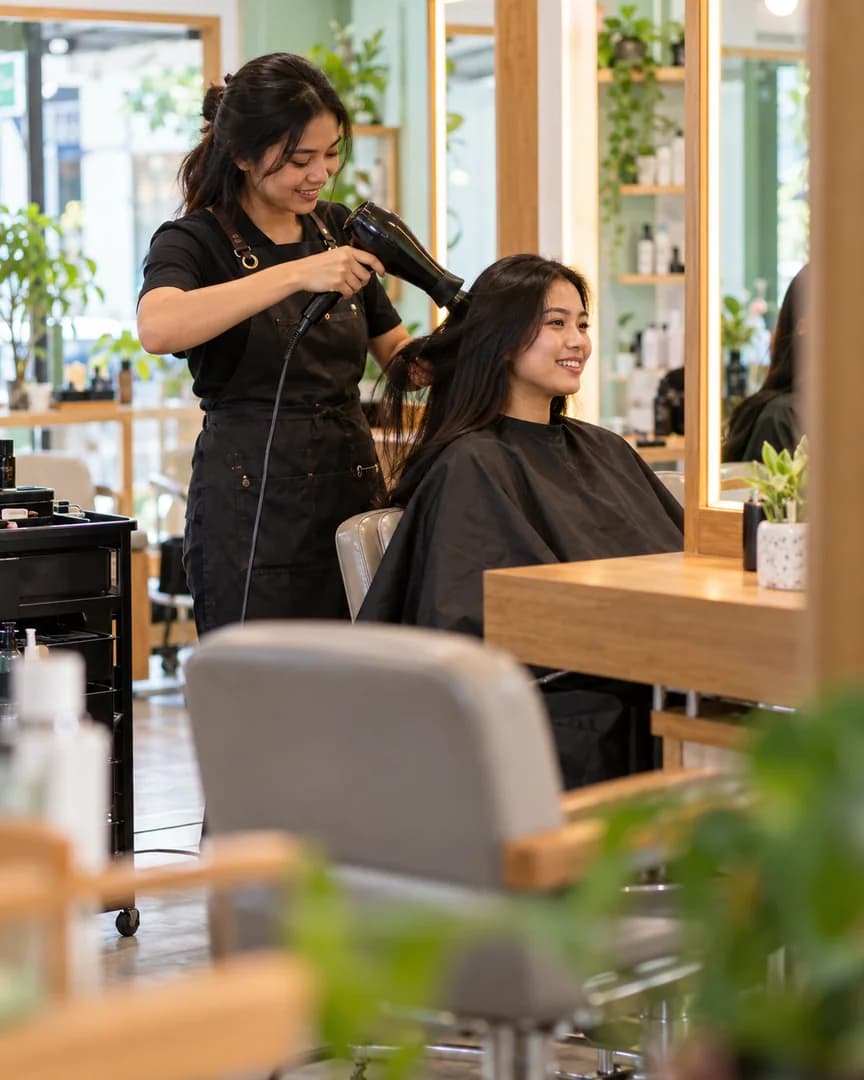 Penata rambut Indonesia mengeringkan rambut pelanggan di salon.
